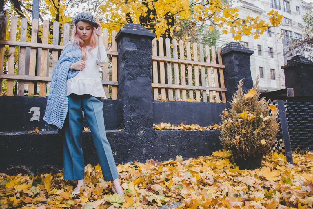 woman standing near fence while stepping on ground covered with withered leaves