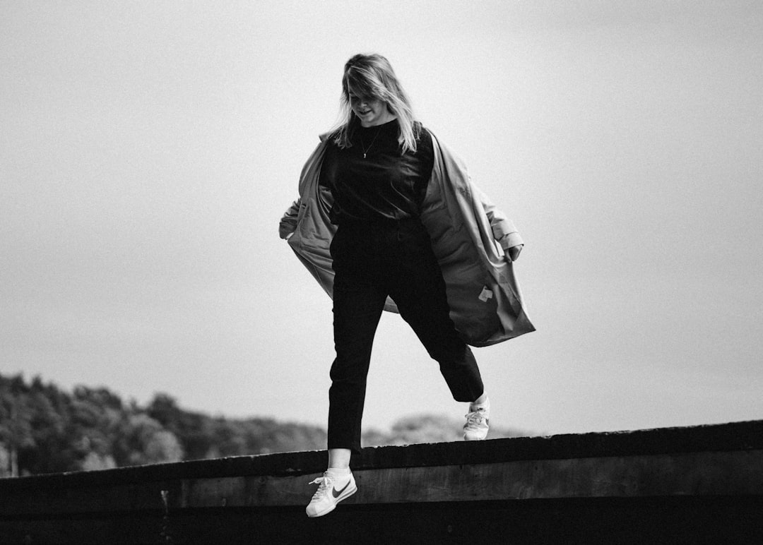 woman in black jacket and pants standing on wooden fence
